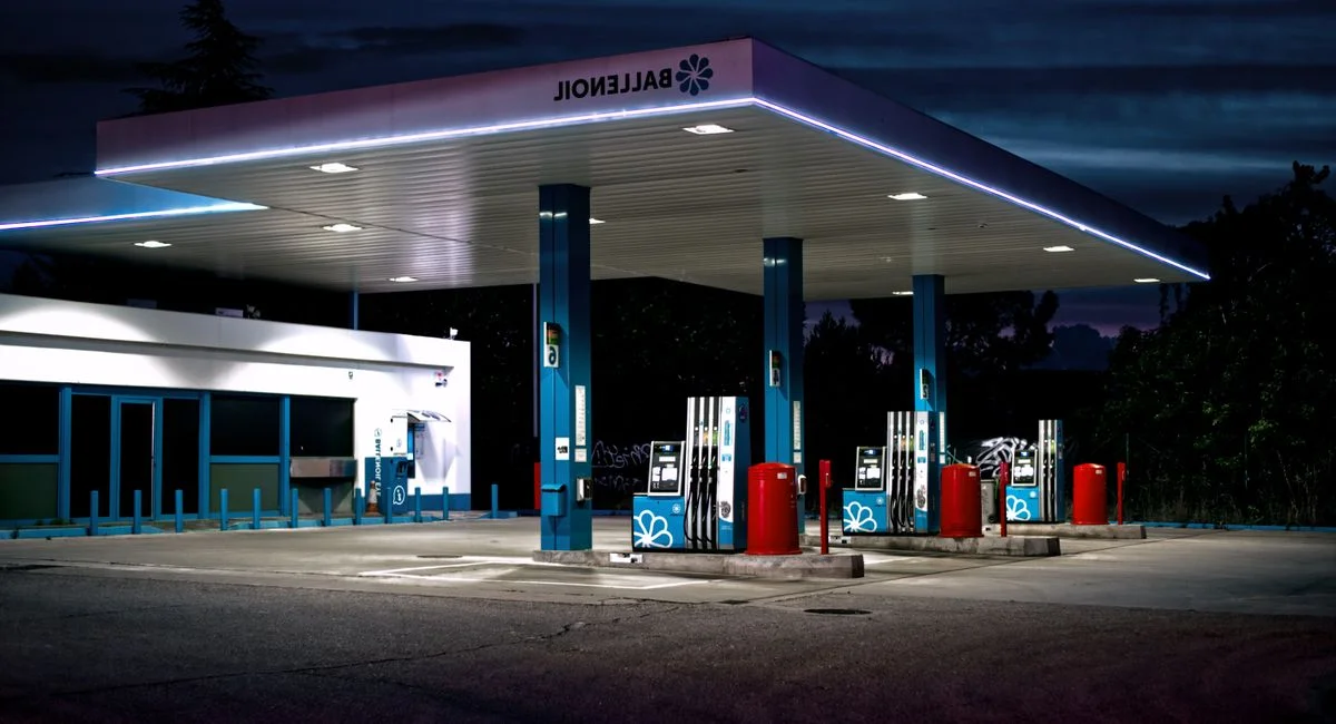 Main posant un pistolet à essence sur une voiture, station-service en arrière-plan