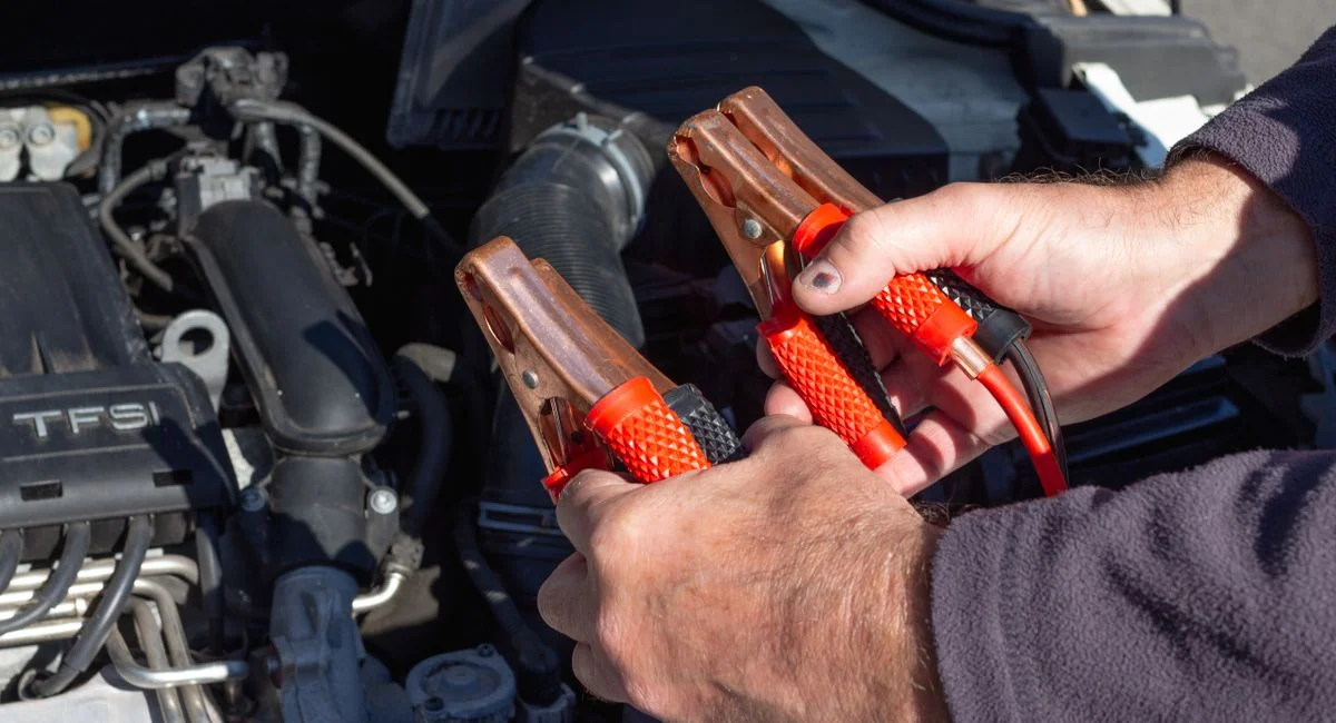 Close-up of hands holding jumper cables near a car engine, ready for repair.